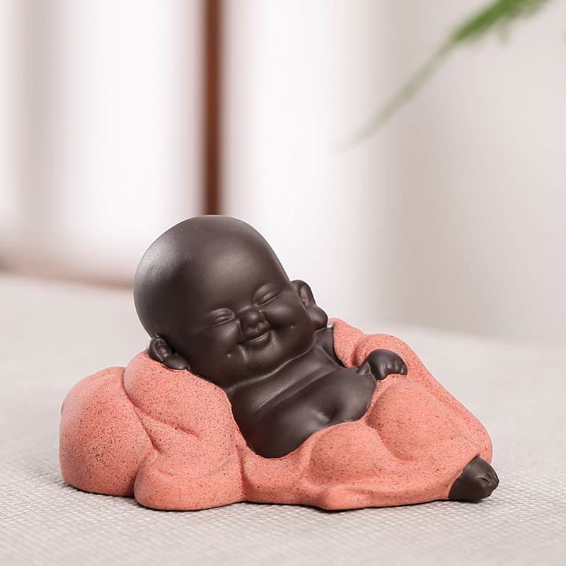 Laughing Buddha Purple Clay Maitreya Statue – reclining Buddha on lavender cushion, dark smooth body against fuzzy purple fabric, calming whimsical decor