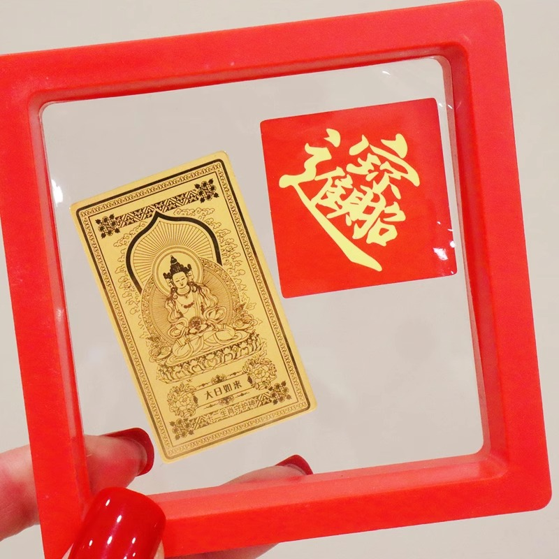 Guardian Gods Gold Foil Phone Sticker – Mahavairocana gold foil sticker inside red display frame next to red 'Wealth' calligraphy sticker, hand-held gift packaging shot
