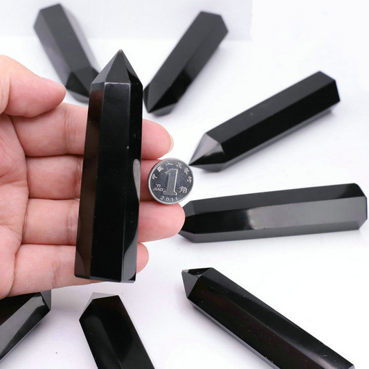Hand holding black obsidian crystal point with coin for size reference, multiple points on white background, energy shield stone