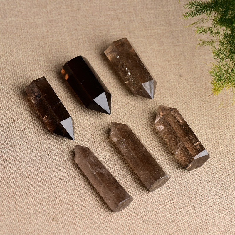 Six natural smoky quartz crystal points arranged on beige fabric, green plant accent, grounding protection stone towers