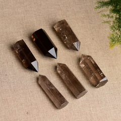 Six natural smoky quartz crystal points arranged on beige fabric, green plant accent, grounding protection stone towers