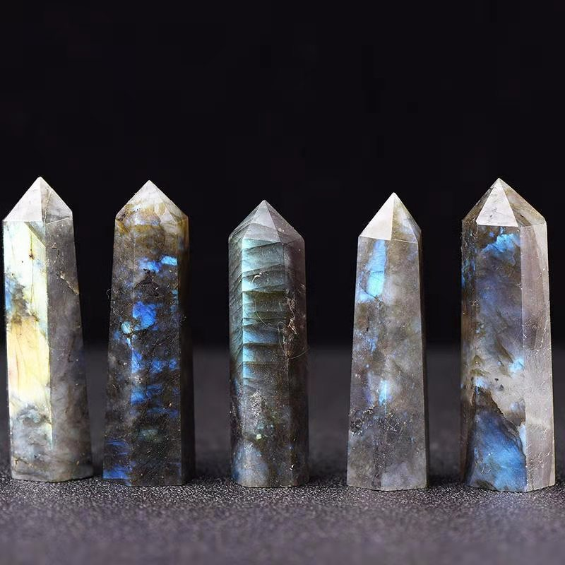 Five natural labradorite crystal pillars arranged in a row, black background, hexagonal tower points with labradorescence