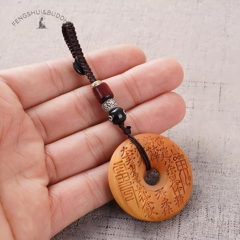 Peach Wood Bagua Coin – hand holding coin showing scale, front spell engraving, brown cord with red silver beads, protection charm