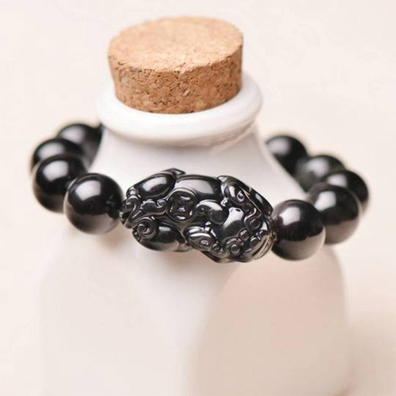 PiXiu Obsidian Bracelet – Draped on white ceramic bottle showing black beads and PiXiu detail