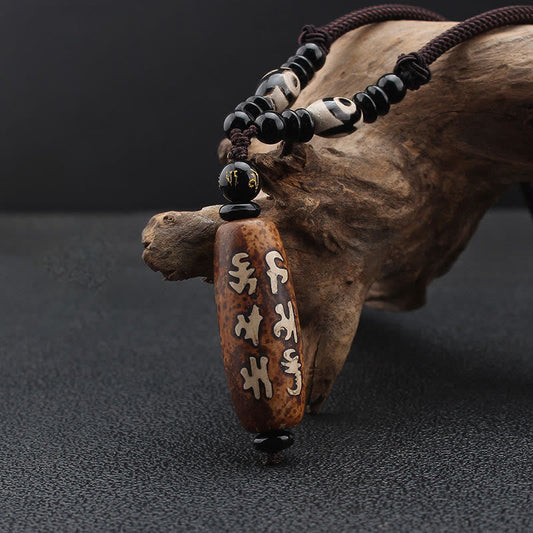 Dzi Bead Necklace – Brown mantra pendant with black onyx accents resting on natural driftwood, mindful
