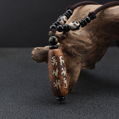 Dzi Bead Necklace – Brown mantra pendant with black onyx accents resting on natural driftwood, mindful