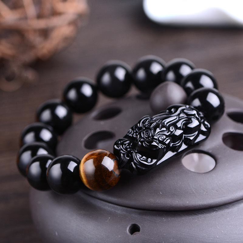 Natural Black Obsidian PiXiu Bracelet on gray ceramic stand, carved guardian beast, wicker background, healing