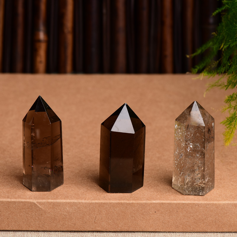 Three natural smoky quartz crystal points on brown surface, varying transparency and inclusions, grounding stone towers