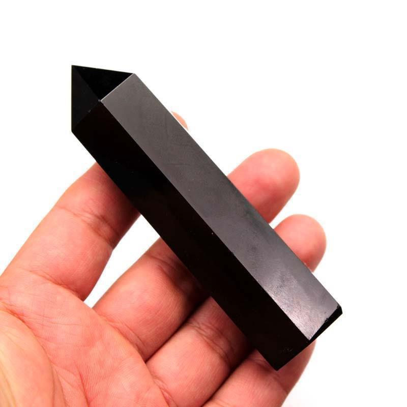 Hand holding polished black obsidian hexagonal crystal point, white background, side angle view, energy shield tower