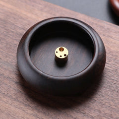 Ebony wood incense bowl with multi-hole brass insert on light wood, mindful