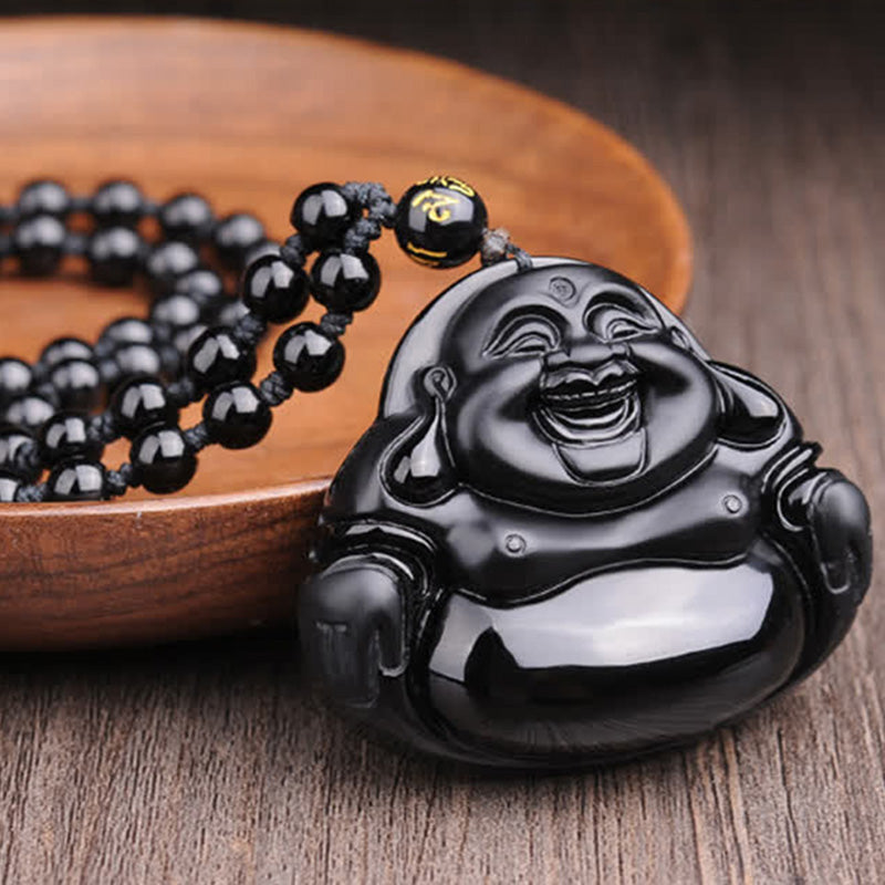 Black Obsidian Laughing Buddha Pendant – on wooden plate with prayer beads spread around, spiritual wellness