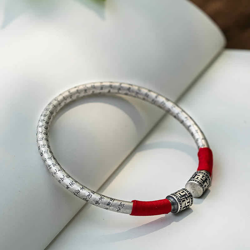 Tibetan Red String Bracelet – silver bangle on book page with botanical background, red thread accent
