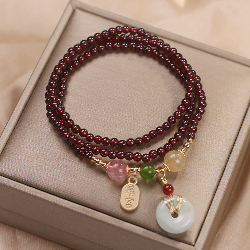 Garnet triple-strand bracelet with bai fu prosperity gold tag charm and white jade peace buckle bi disc pendant in gold wire cage setting on champagne satin presentation box