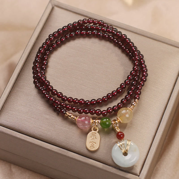 Garnet triple-strand bracelet with bai fu prosperity gold tag charm and white jade peace buckle bi disc pendant in gold wire cage setting on champagne satin presentation box