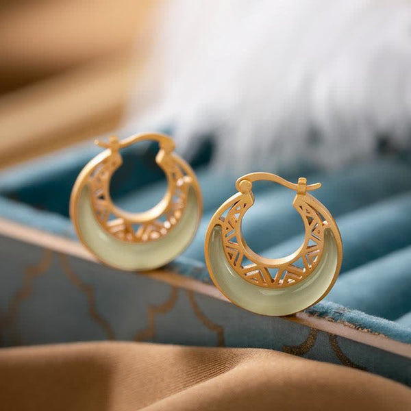 Crescent Moon Jade Drop Earrings – Gold openwork hoop earrings with white crescent-shaped jade inlay and geometric lattice cutouts on teal velvet, side angle