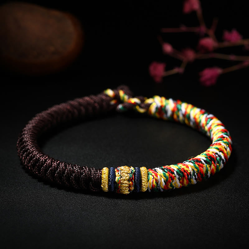 Red and burgundy Tibetan king kong knot bracelet with gold focal accent multicolor spiral braid section and navy blue decorative bands on dark background