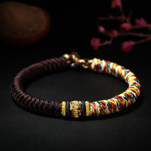 Red and burgundy Tibetan king kong knot bracelet with gold focal accent multicolor spiral braid section and navy blue decorative bands on dark background