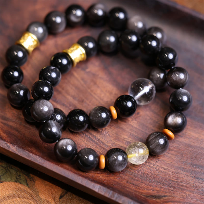 Silver Sheen Obsidian Mantra Bracelet – angled view on wood tray with obsidian beads and gold accent, healing jewelry