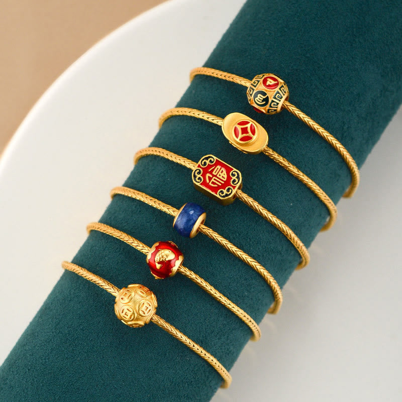 18K Gold Om Mani Padme Hum Koi Fish Bracelet – six gold cord bracelets with varied enamel charms on green velvet stand, overhead view
