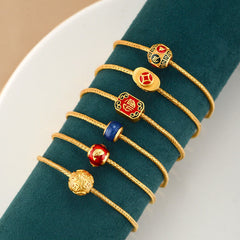 18K Gold Om Mani Padme Hum Koi Fish Bracelet – six gold cord bracelets with varied enamel charms on green velvet stand, overhead view