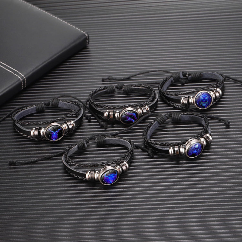 Zodiac Leather Wrap Bracelet – five zodiac bracelets clustered on dark surface with leather notebook