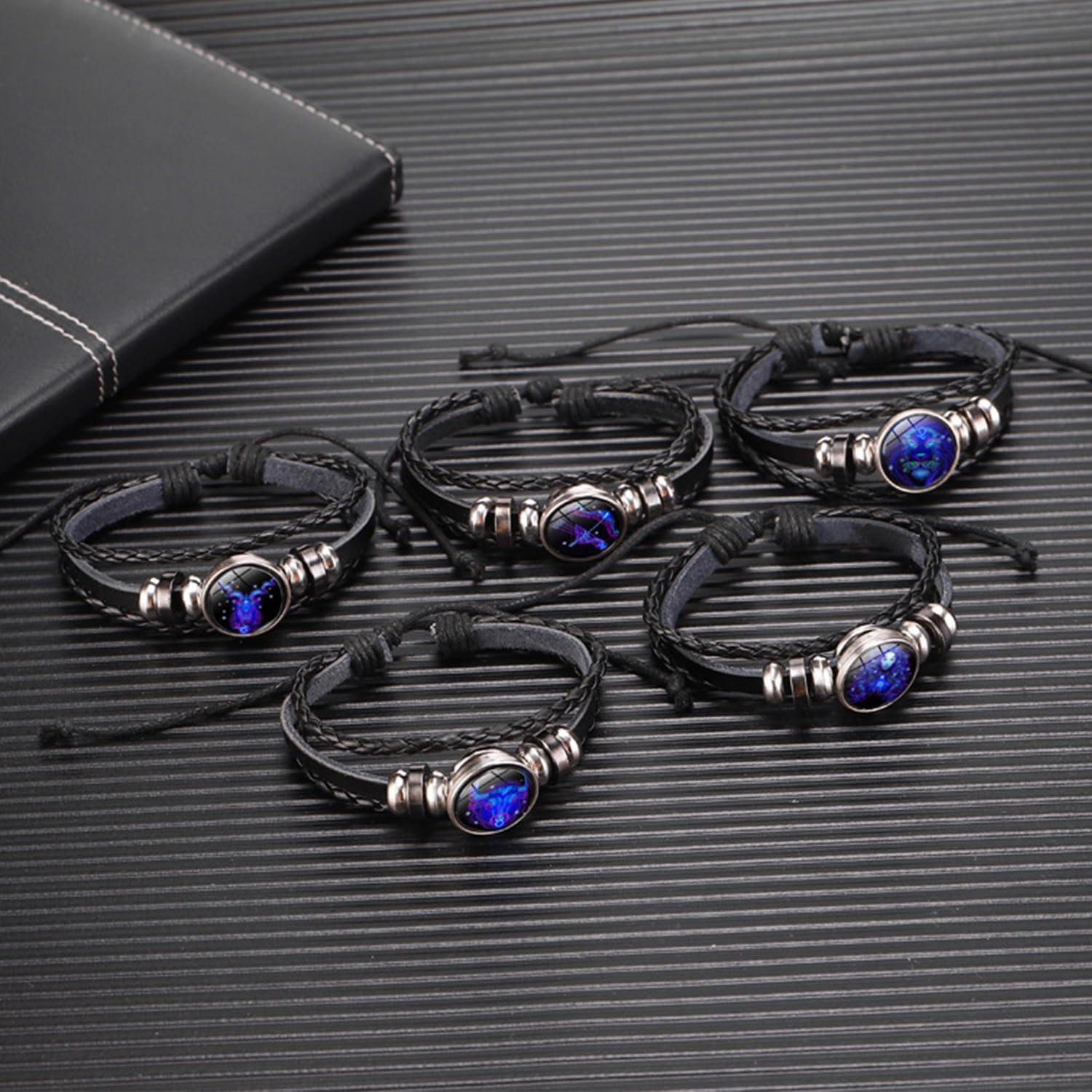 Zodiac Leather Wrap Bracelet – five zodiac bracelets clustered on dark surface with leather notebook