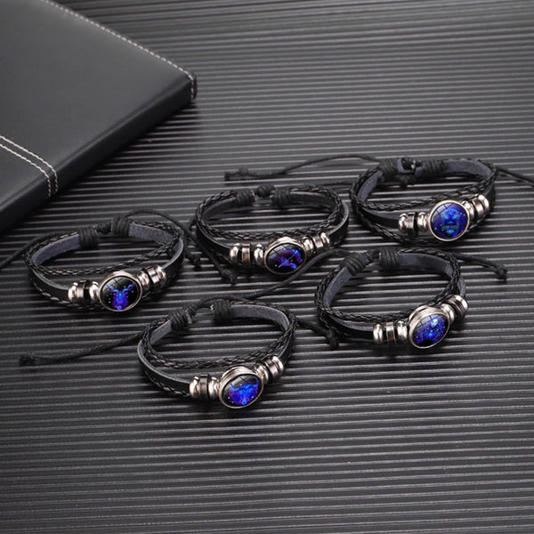 Zodiac Leather Wrap Bracelet – five zodiac bracelets clustered on dark surface with leather notebook