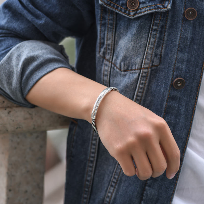 Tibetan Heart Sutra Cuff Bracelet – worn with rolled denim sleeve, stone ledge backdrop, silver cuff detail
