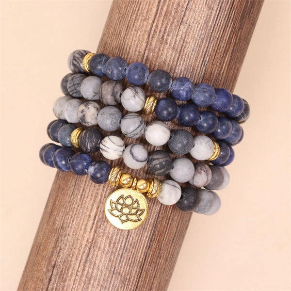 Stack of four sodalite and zebra jasper wrap bracelets on wooden display stand showing blue marbled gray and charcoal bead combinations with gold lotus flower charm and ridged metal spacers
