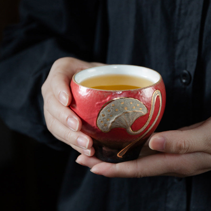 Lotus Pod Ceramic Kung Fu Tea Cup - Red cup cradled in hands with amber tea, contemplative