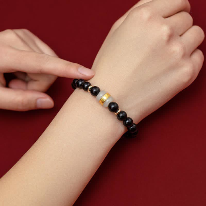 Black Obsidian Jade Bracelet – Worn on wrist against burgundy backdrop with hand pointing at beads