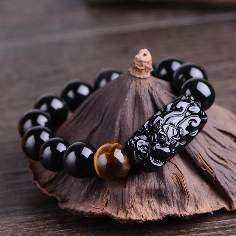 Black Obsidian PiXiu Bracelet with Tiger Eye bead on lotus pod, dark wood background, feng shui wealth jewelry