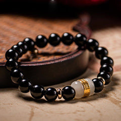 Black Obsidian Jade Bracelet – Elevated view on warm toned surface highlighting gold metalwork and jade accent bead