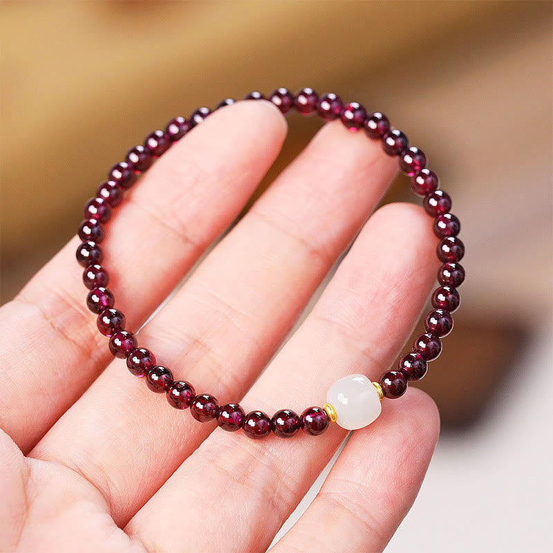 Hand-worn natural garnet jade bracelet showing deep red garnet beads with white jade focal bead on wrist, feminine everyday jewelry lifestyle shot