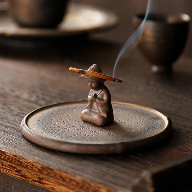Ceramic Meditating Figure Incense Burner with rising smoke on wood table, mindful