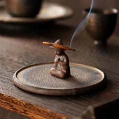 Ceramic Meditating Figure Incense Burner with rising smoke on wood table, mindful