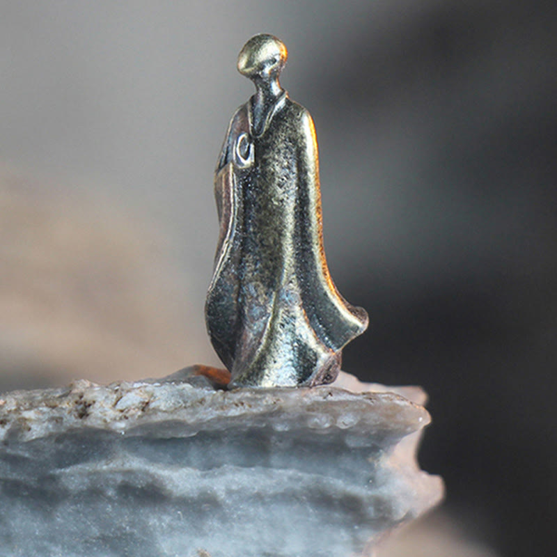 Mini Metal Meditation Buddha Decoration – single standing bronze monk figurine close-up on rock, meditative focus
