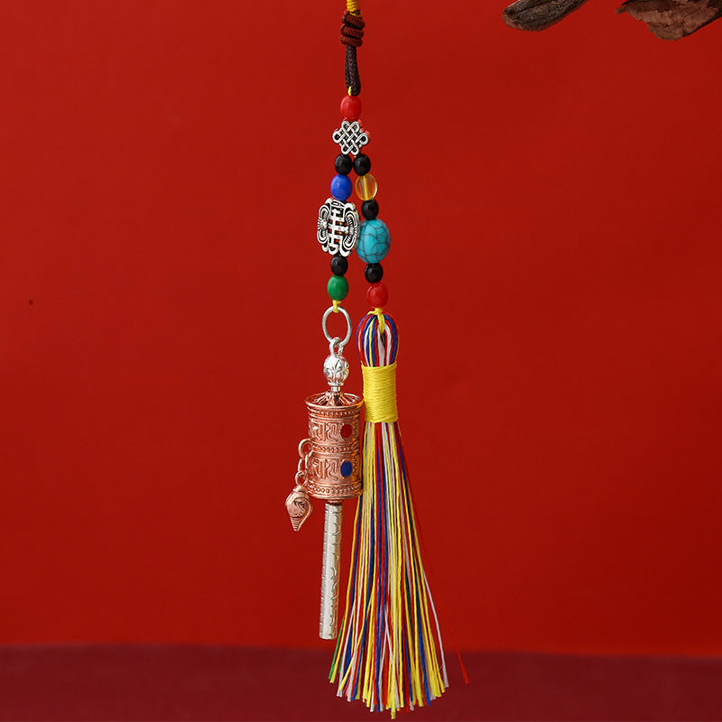 Tibetan Prayer Wheel Keychain – antique copper-tone prayer wheel pendant with colorful silk tassel, turquoise beads and auspicious knot charm, red background, front vertical view