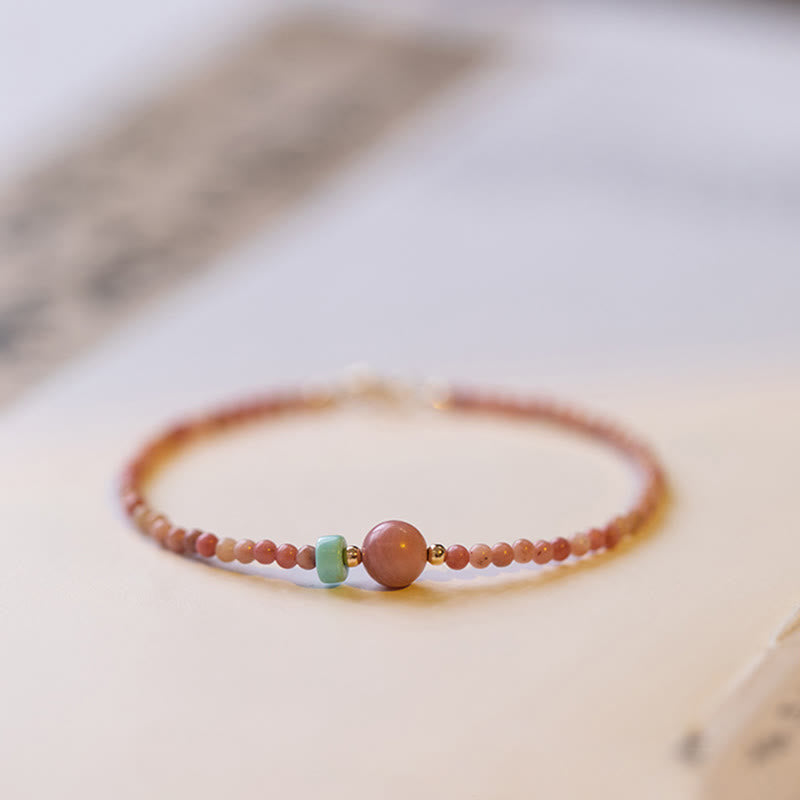 Rhodonite Loving Energy Bracelet – Pink stone beads with rose focal bead and blue accent, watercolor cream and blue wash background, low side angle