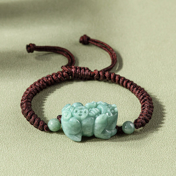 Jade PiXiu Knot Bracelet – Dark red braided cord bracelet with light green jade PiXiu on beige surface