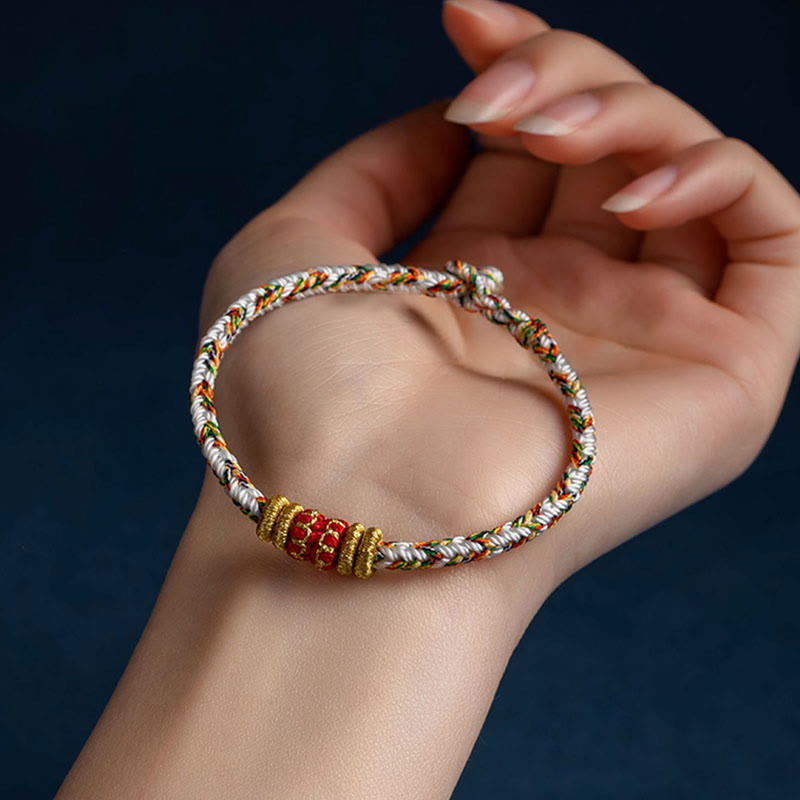 Multicolor braided cord bracelet with white base, red centerpiece bead and gold spacers worn on woman's wrist, adjustable handmade bohemian friendship jewelry