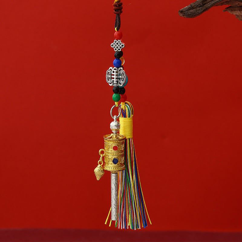 Tibetan Prayer Wheel Keychain – five assorted metal-tone prayer wheel pendants with colorful tassels and beads laid flat on deep red background, collection overview shot