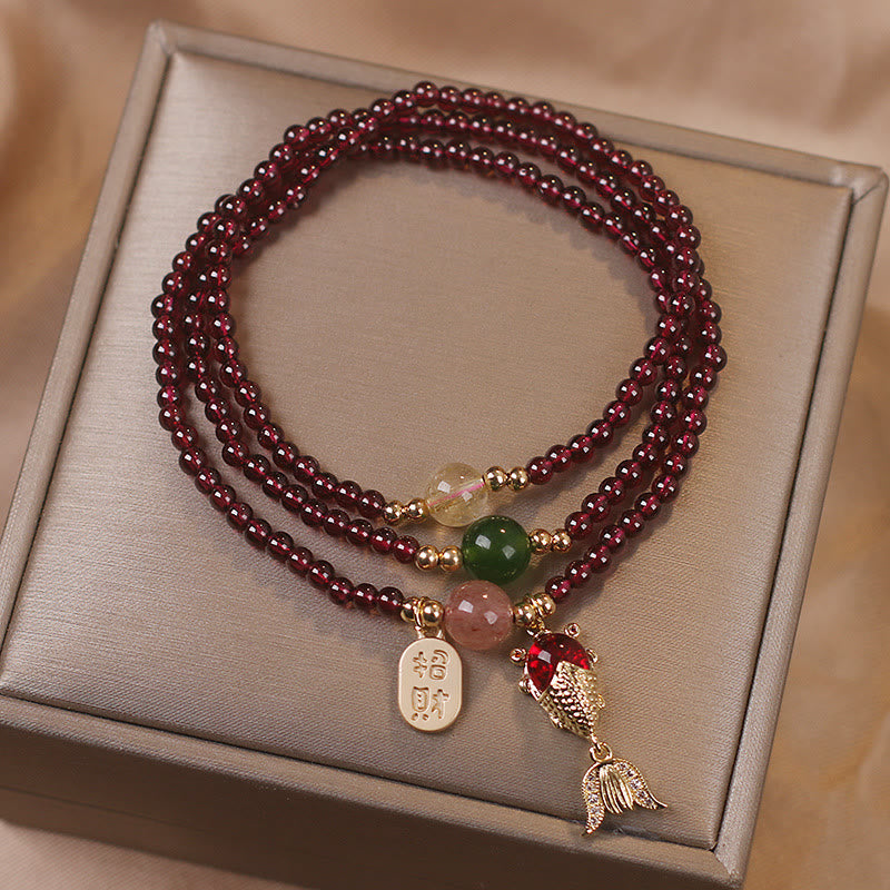 Triple-strand garnet bracelet with gold koi fish charm red gemstone body articulated fin details and zhao cai wealth Chinese character tag on champagne jewelry box