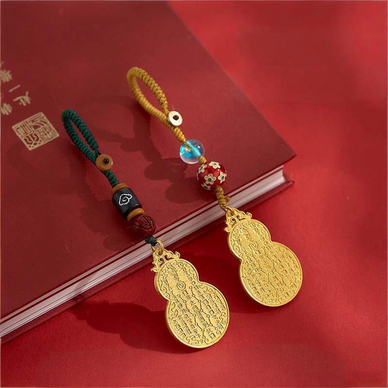 Two antique gold gourd keychains with green and gold cords on red book