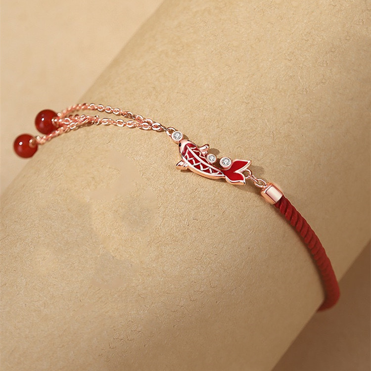 Shang An Koi Anklet – wrist close-up showing red koi charm with crystals and red bead tassels on rose gold chain, luxury