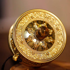 Sandalwood Tibetan Prayer Wheel – Top-down view of brass prayer wheel on carved wood stand, filigree patterns, warm studio...
