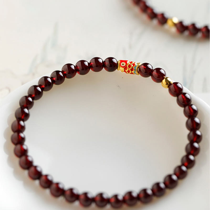 999 Gold Koi Fish Bracelet – flat lay on marble surface, garnet beads visible, koi fish charm bracelet