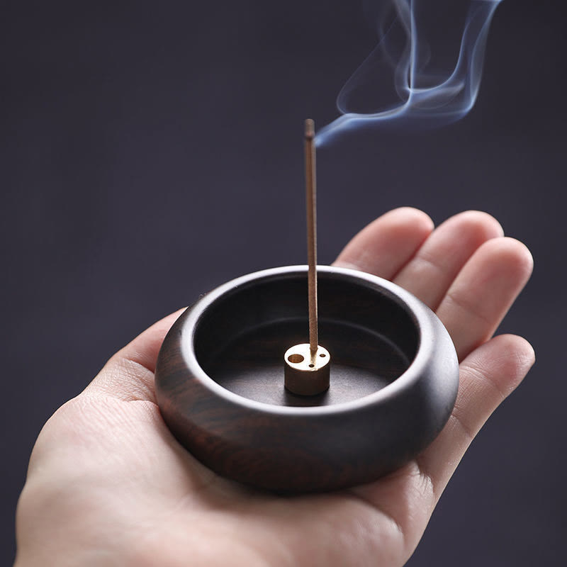 Dark wood incense holder with brass fitting and smoke held in hand, healing