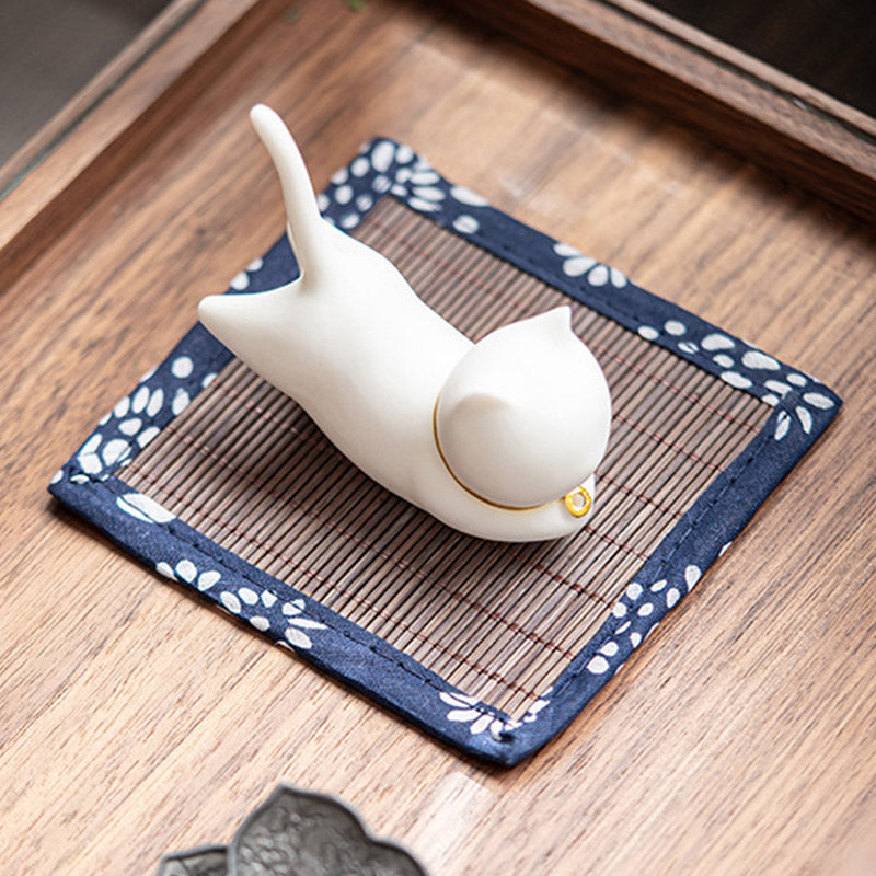 White ceramic cat figurine with gold collar on woven bamboo mat, zen decor