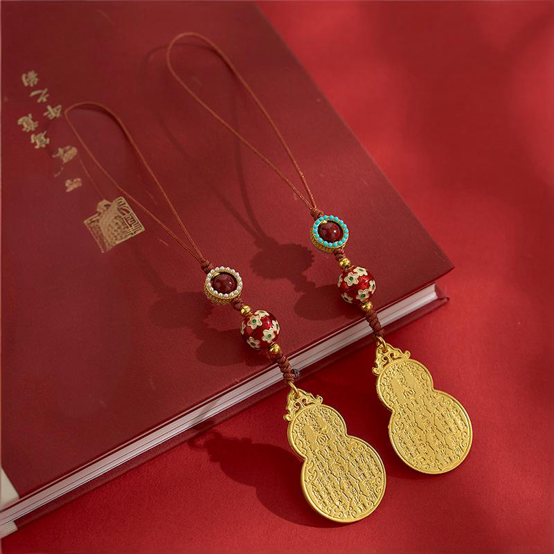 Two antique gold gourd charms with decorative beads side by side on red book
